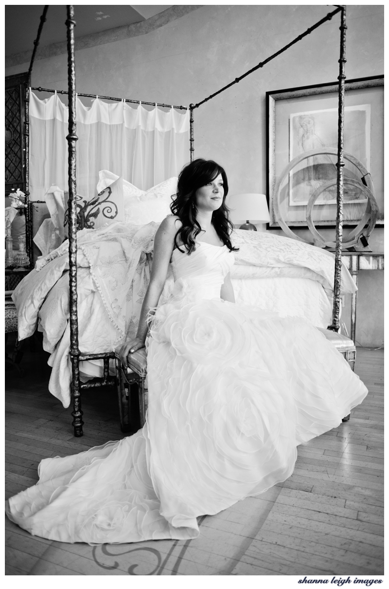 Beautiful bride Emily in her custom wedding dress by Bliss Bridal of Fort Worth, Texas posing for her bridal portraits at the gorgeous vintage styled Iron Bed store in Frisco, Texas in front of a canopy bed with her beautiful brunette loose curls.