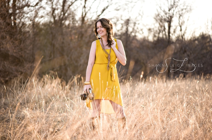 A photographer posing with her Canon camera in a mustard colored dress with Frye Jane boots in an overgrown field.