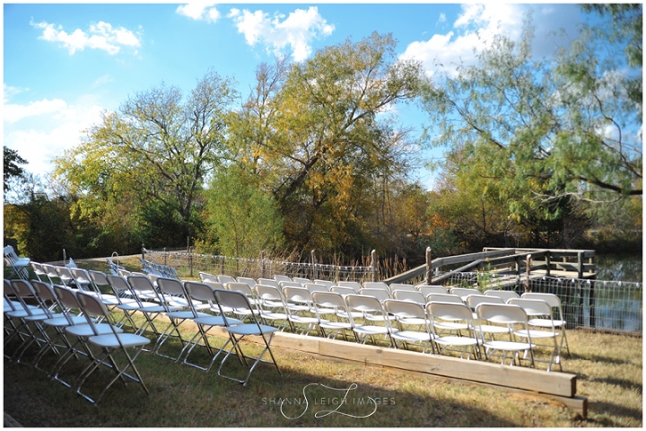 White chairs set up in front of the water before an outdoor wedding ceremony at Wildscape Ranch in Mansfield, Texas.